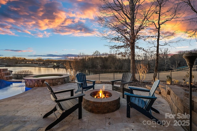 patio terrace at dusk with a water view, pool water feature, a pool with hot tub, and a fire pit