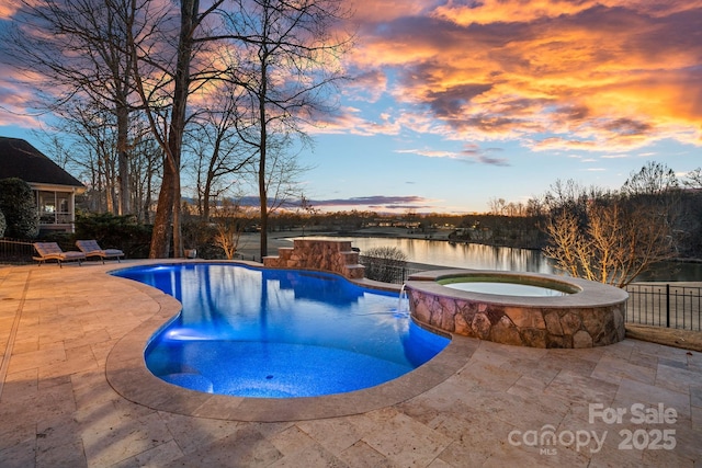 pool at dusk with a patio, a water view, pool water feature, and an in ground hot tub