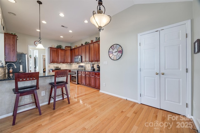 kitchen with appliances with stainless steel finishes, lofted ceiling, tasteful backsplash, and decorative light fixtures