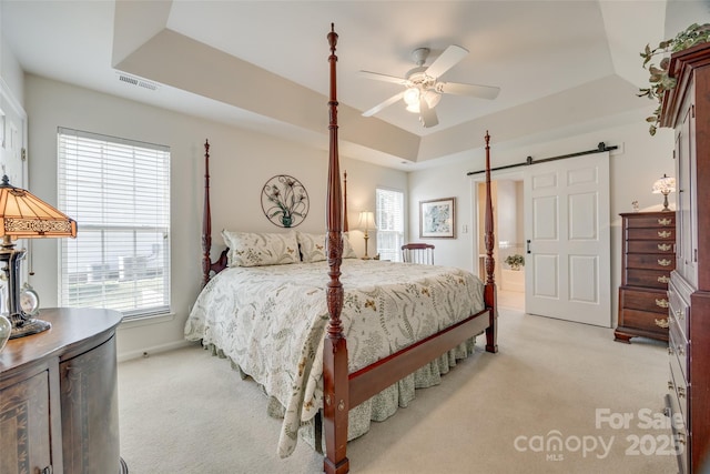 bedroom with light colored carpet, ceiling fan, a barn door, and a raised ceiling