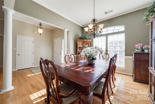 dining space featuring an inviting chandelier, crown molding, light hardwood / wood-style floors, and decorative columns