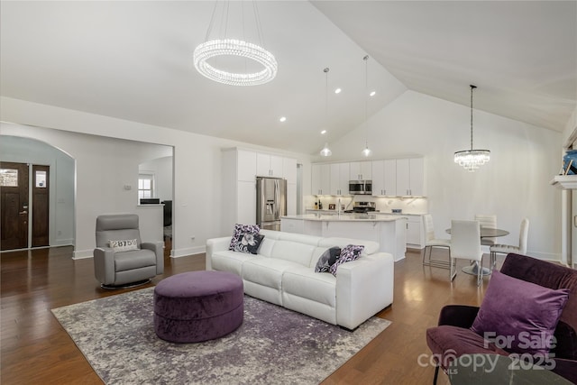 living room featuring dark wood-type flooring, a chandelier, and high vaulted ceiling