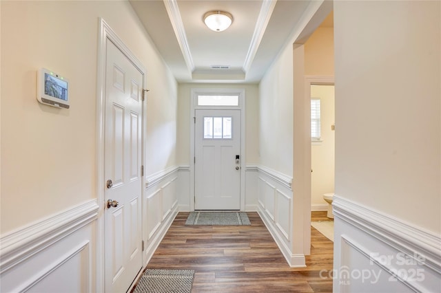 doorway featuring dark wood-type flooring, a tray ceiling, and ornamental molding