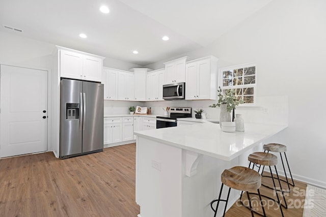 kitchen with a breakfast bar, white cabinetry, light hardwood / wood-style flooring, appliances with stainless steel finishes, and kitchen peninsula