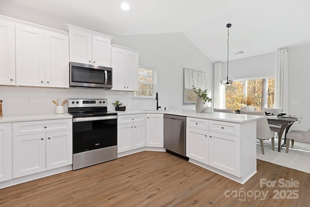 kitchen with appliances with stainless steel finishes, white cabinetry, hanging light fixtures, decorative backsplash, and kitchen peninsula