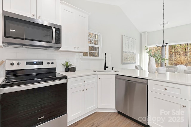 kitchen featuring pendant lighting, lofted ceiling, sink, white cabinets, and stainless steel appliances