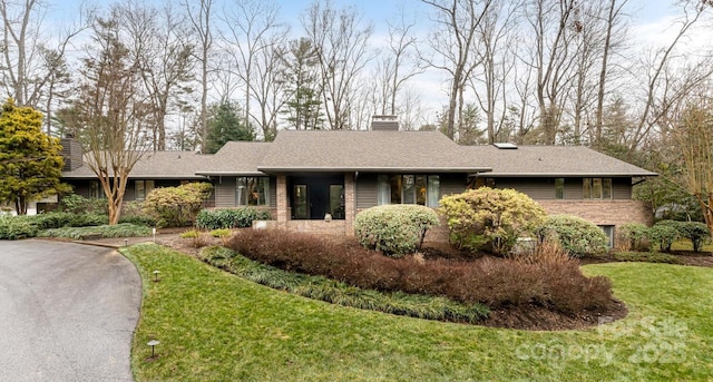 single story home featuring brick siding, a shingled roof, a chimney, and a front yard