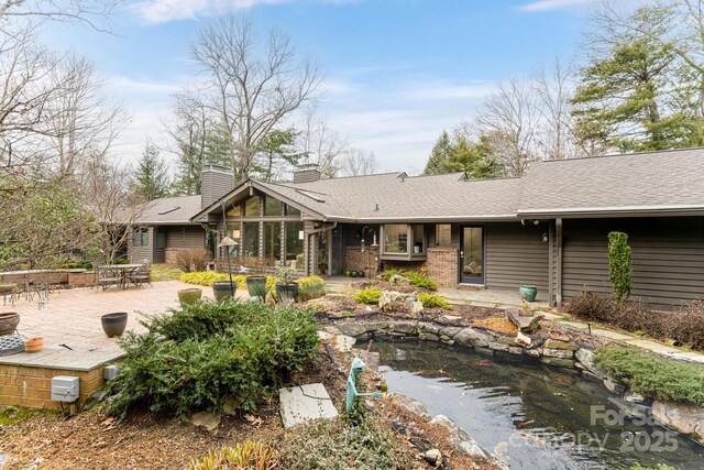 back of house featuring a chimney, a sunroom, a patio area, a garden pond, and outdoor dining space