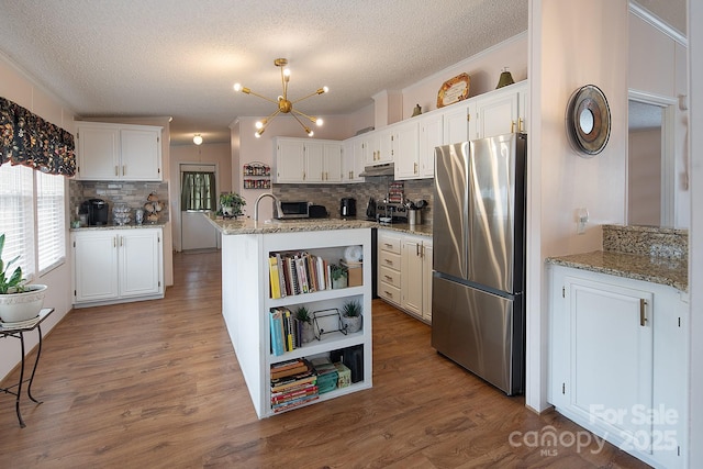 kitchen featuring a kitchen island with sink, light stone counters, stainless steel fridge, and white cabinets