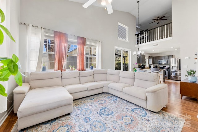 living room featuring ceiling fan with notable chandelier, wood-type flooring, and vaulted ceiling