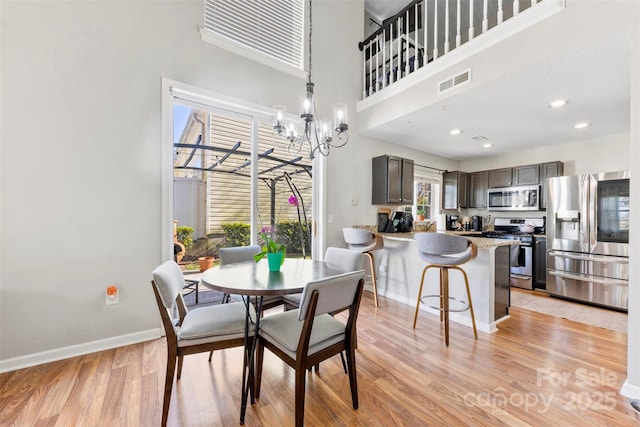 dining space with a healthy amount of sunlight, a high ceiling, a notable chandelier, and light hardwood / wood-style floors