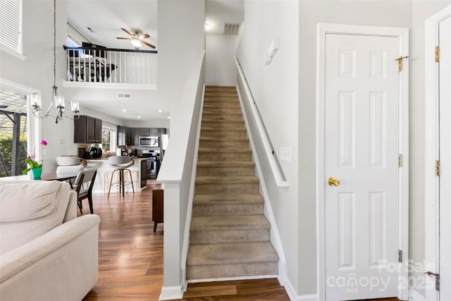 staircase with wood-type flooring, ceiling fan with notable chandelier, and a towering ceiling