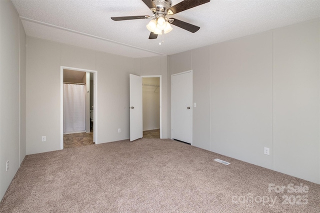 unfurnished bedroom featuring a spacious closet, a textured ceiling, carpet floors, a closet, and ceiling fan