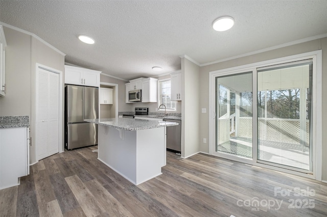 kitchen with appliances with stainless steel finishes, white cabinets, light stone countertops, a textured ceiling, and a kitchen island