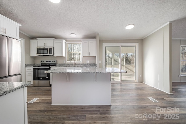 kitchen with light stone countertops, white cabinets, appliances with stainless steel finishes, and crown molding