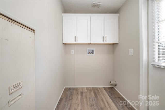 washroom with a textured ceiling, hookup for a washing machine, light hardwood / wood-style floors, and cabinets