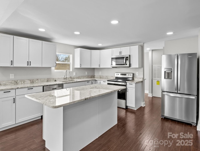 kitchen with appliances with stainless steel finishes, white cabinetry, sink, a kitchen island, and light stone counters