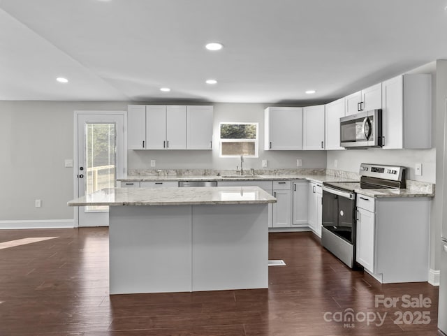 kitchen with light stone countertops, white cabinets, a center island, stainless steel appliances, and sink