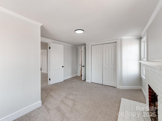 unfurnished bedroom with a closet, a brick fireplace, light colored carpet, and crown molding