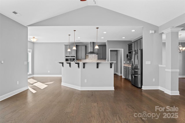 kitchen featuring appliances with stainless steel finishes, wall chimney exhaust hood, lofted ceiling, decorative light fixtures, and backsplash