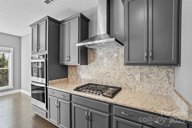 kitchen with appliances with stainless steel finishes, wall chimney range hood, light stone counters, and gray cabinets