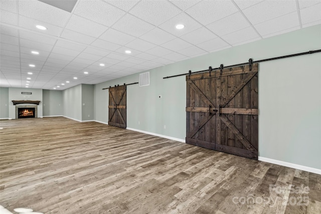 unfurnished living room featuring a paneled ceiling, a barn door, and wood-type flooring