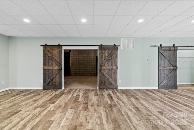 unfurnished room with wood-type flooring, a drop ceiling, and a barn door