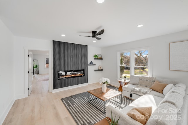 living room with a large fireplace, ceiling fan, and light wood-type flooring