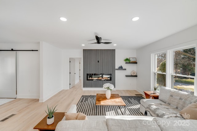 living room featuring ceiling fan, a barn door, and light hardwood / wood-style flooring