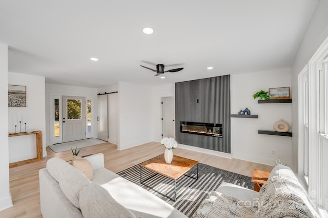 living room with a fireplace, a barn door, ceiling fan, and light wood-type flooring