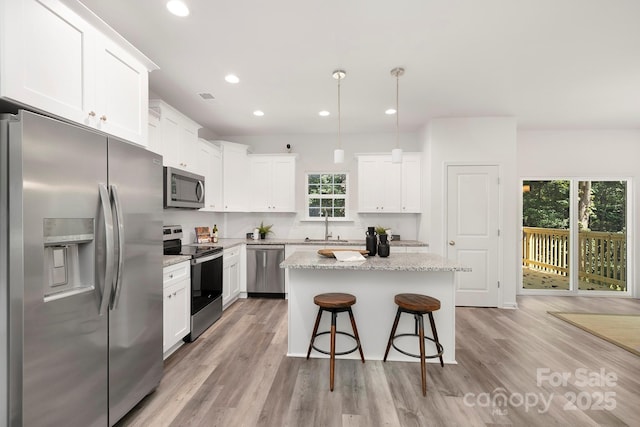 kitchen with a center island, light stone countertops, appliances with stainless steel finishes, white cabinetry, and hanging light fixtures