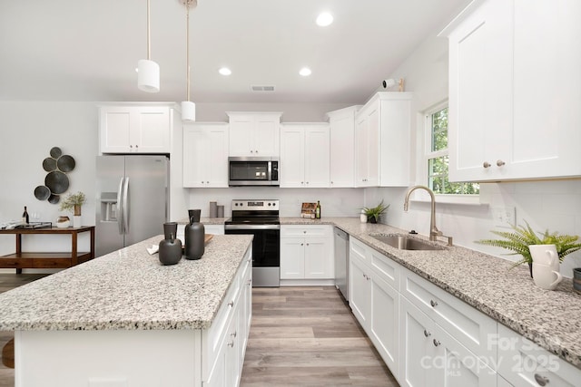 kitchen featuring hanging light fixtures, appliances with stainless steel finishes, sink, white cabinets, and a center island