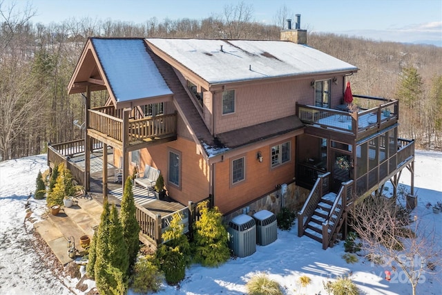 snow covered back of property with a wooden deck, a balcony, and central air condition unit