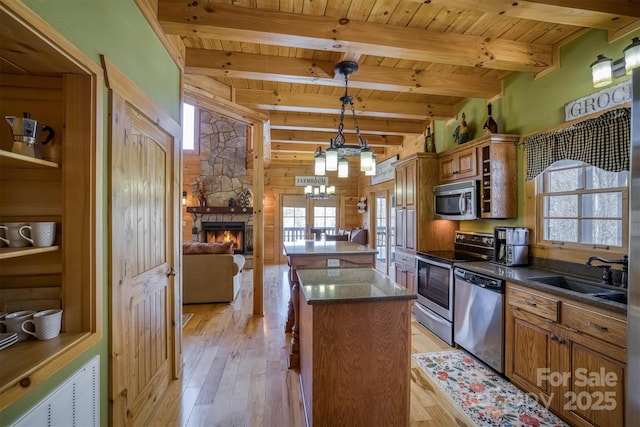 kitchen with stainless steel appliances, decorative light fixtures, a kitchen island, beam ceiling, and sink