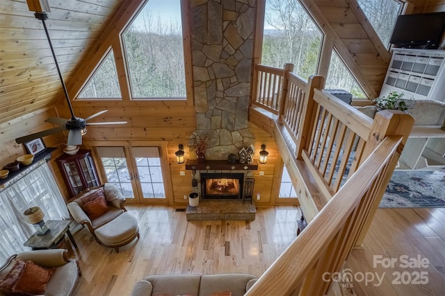 living room featuring a stone fireplace, wooden walls, a high ceiling, and light hardwood / wood-style flooring