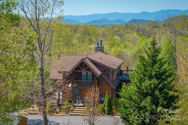 view of front of house with a mountain view, a chimney, a forest view, and a balcony