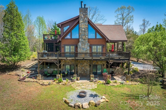 back of house featuring a patio, a chimney, stone siding, and a lawn