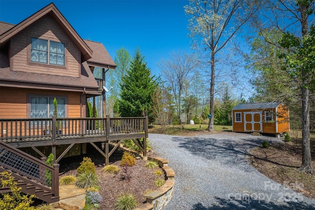 view of property exterior featuring a deck, a storage shed, an outdoor structure, roof with shingles, and gravel driveway