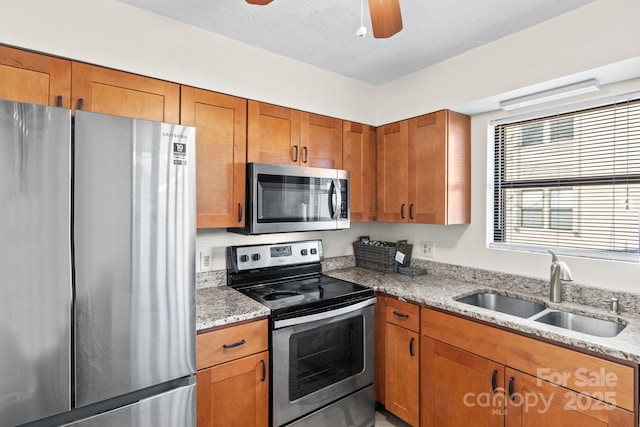 kitchen featuring sink, ceiling fan, stainless steel appliances, light stone countertops, and a textured ceiling