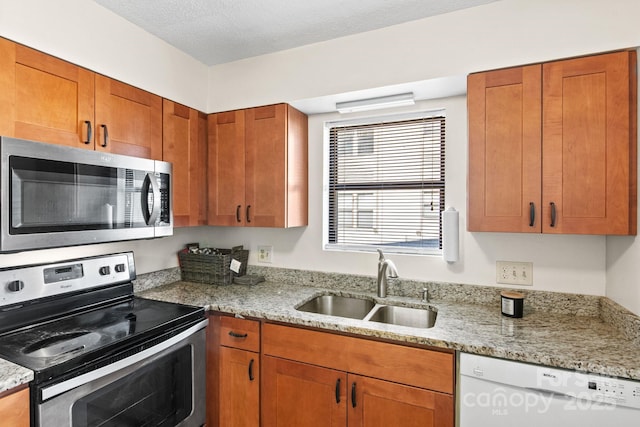 kitchen featuring stainless steel appliances, light stone countertops, sink, and a textured ceiling