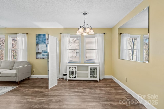 unfurnished dining area featuring an inviting chandelier, plenty of natural light, hardwood / wood-style floors, and a textured ceiling