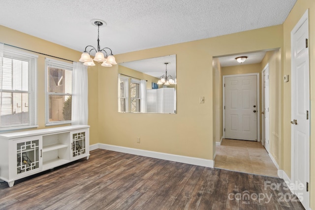 unfurnished dining area featuring wood-type flooring, a textured ceiling, and a notable chandelier