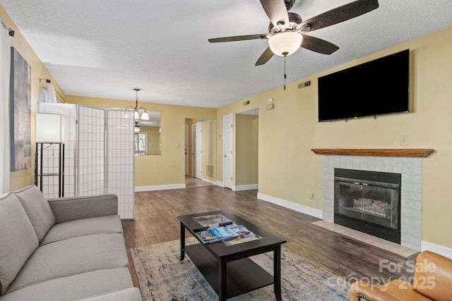 living room with a tiled fireplace, ceiling fan with notable chandelier, dark hardwood / wood-style flooring, and a textured ceiling