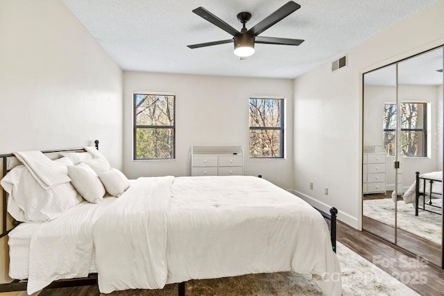 bedroom with wood-type flooring, a textured ceiling, a closet, ceiling fan, and multiple windows