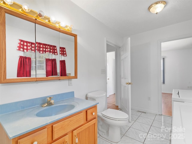 bathroom with a textured ceiling, washer / dryer, tile patterned floors, vanity, and toilet