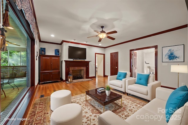 living room featuring a fireplace, light hardwood / wood-style flooring, ceiling fan, and ornamental molding