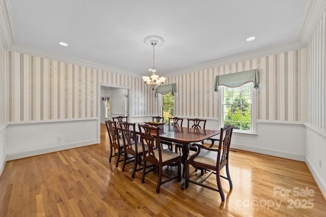 dining space with light wood-type flooring, ornamental molding, and an inviting chandelier