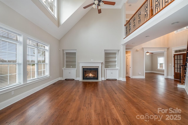 unfurnished living room with a high ceiling, a healthy amount of sunlight, built in features, and ceiling fan