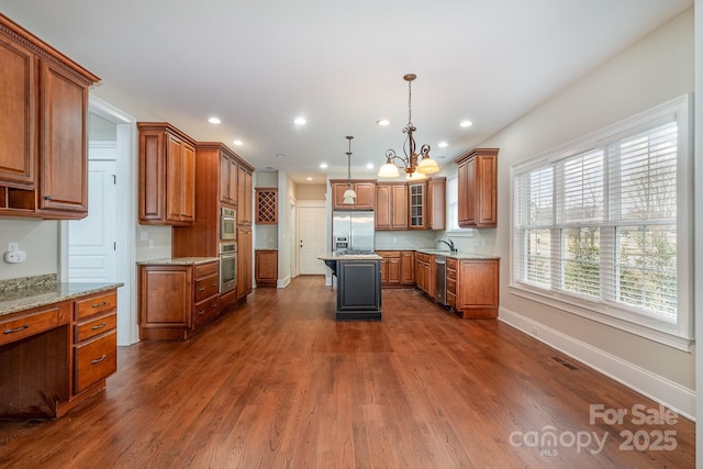 kitchen featuring dark wood-type flooring, appliances with stainless steel finishes, a center island, light stone countertops, and decorative light fixtures