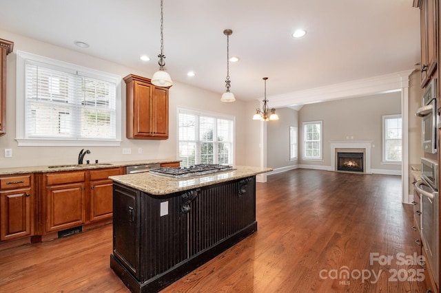 kitchen with sink, hanging light fixtures, light stone counters, wood-type flooring, and a kitchen island